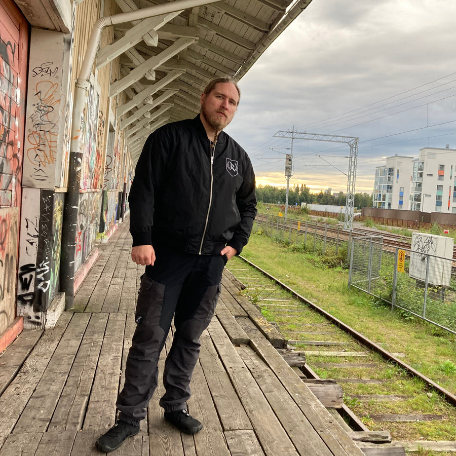 Rurik Fightgear-lentäjänpusakka.
Rurik FG "R" -logo rintapielessä sekä riimulogo selässä monivärisesti brodeerattuna. Kuvassa pilottitakki  Mikan päällä junan laiturilla. ptcombet.com