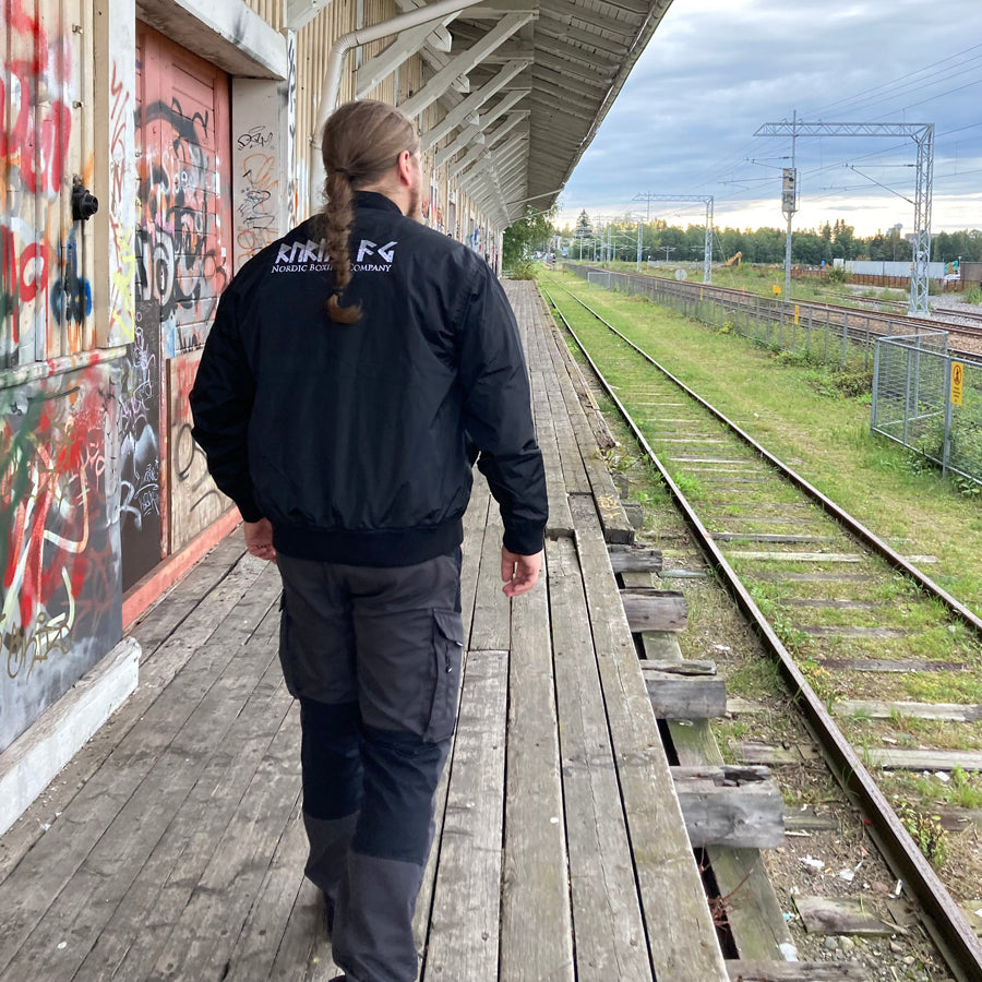 Rurik Fightgear-lentäjänpusakka.
Rurik FG "R" -logo rintapielessä sekä riimulogo selässä monivärisesti brodeerattuna. Kuvassa pilottitakki  Mikan päällä takaa kuvattuna. ptcombet.com